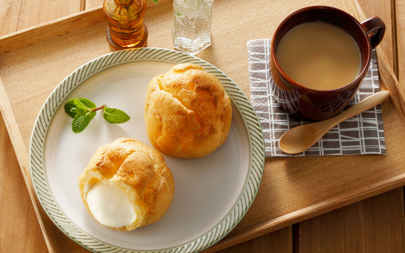 Cream puffs on a plate next to a cup of coffee on a light wood coffee table.